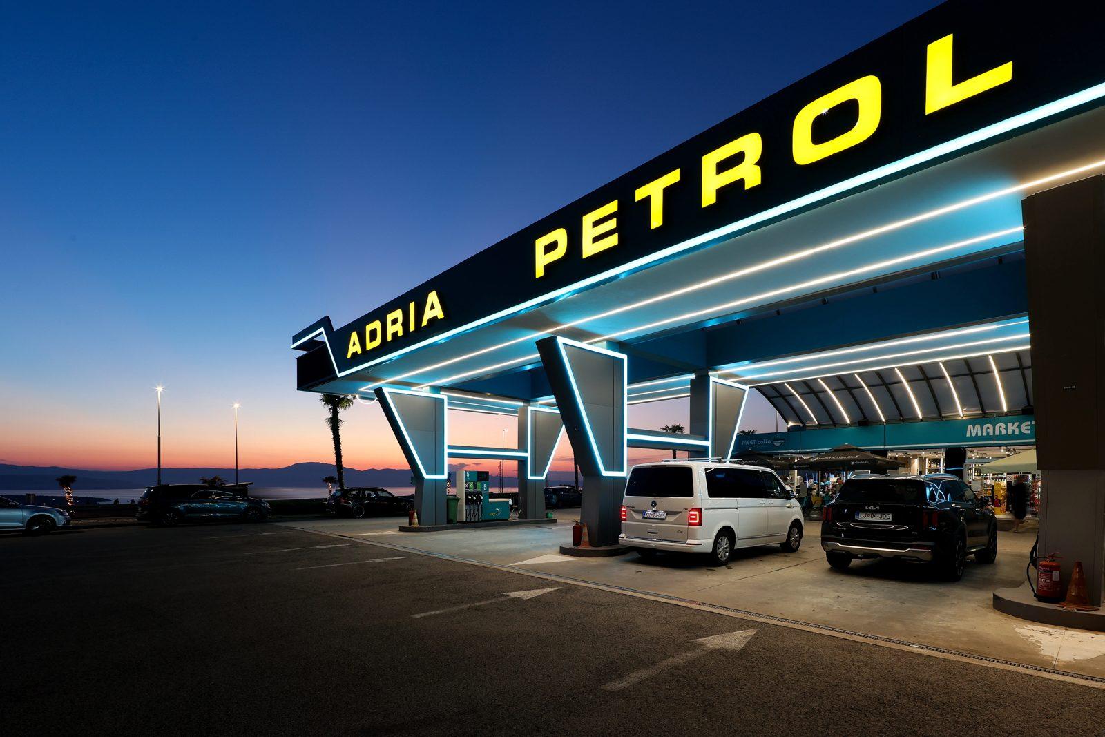 The yellow ADRIA PETROL lettering and neon canopy at blue hour with cars at the pumps