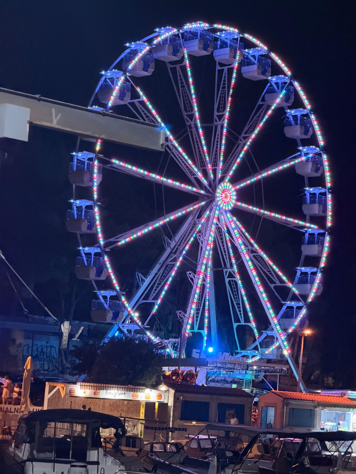 Beleuchtetes Riesenrad am Hafen von Vodice bei Nacht, davor liegen Boote
